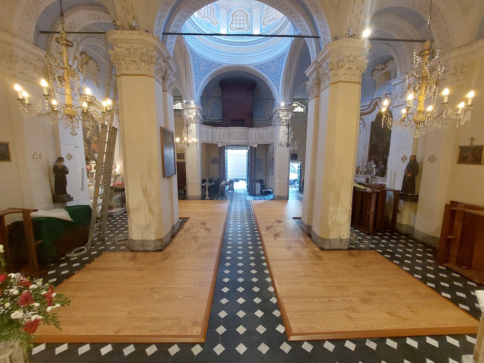 Interno di una chiesa a Imperia con pedana termica in legno installata lungo la navata centrale, lampadari in ottone e colonne decorate